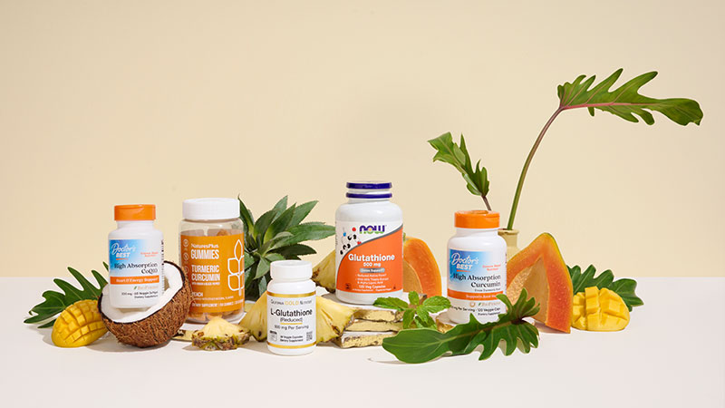 Bottles of supplements, including turmeric and glutathione, are displayed with tropical fruits and leaves on a light background, conveying a fresh, natural vibe.